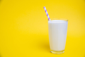 Glass of milk with purple straw isolated on yellow background