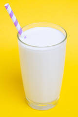 Glass of milk with purple straw isolated on yellow background