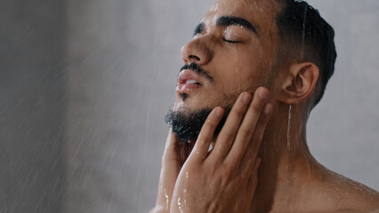 Arab indian man bearded guy naked male washes head with shampoo washing hair face and beard in bathroom showering in at home in hotel after workout close up. Brunette rinsing shampoo and conditioner