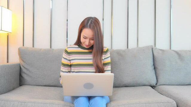 A young woman sitting on a couch works on her laptop with sucess.