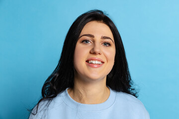 Fototapeta premium Portrait of young beautiful girl with long glossy dark hair posing isolated on blue background. Concept of emotions, facial expression