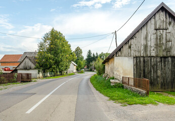 Driving on a Provincial Road through Villages in Croatian Countryside. Rural Scenery with Green Trees and Old Cottages on a Sunny Day.