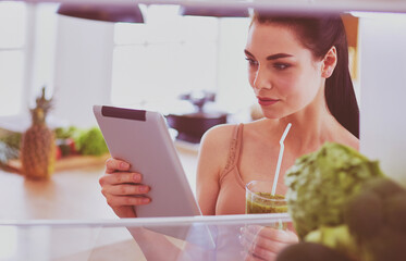 Young woman with glass of tasty healthy smoothie at table in kitchen