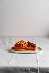 Home baked orange and cinnamon pound cake on a plate on a table clad with white tablecloth