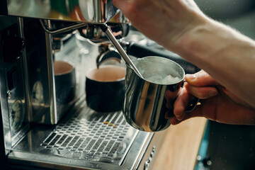 Process of preparing milk foam for cappuccino, heating and whipping. Barista controls temperature by holding pitcher in his hands