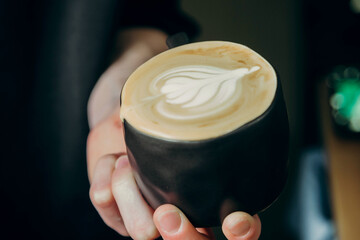 Close-up of a guy holding a black cup of coffee with latte art
