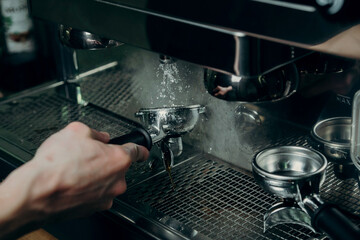 Steamed coffee machine, barista rinses tamper with hot water from coffee machine