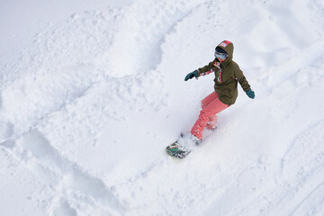 girl in helmet with glasses and tracksuit snowboarding down the mountain
