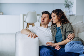 Fototapeta na wymiar Happy newlyweds with dark hair sit on comfortable sofa in living room and discuss plans for future smiling broadly closeup