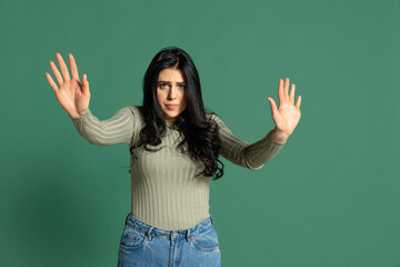 Portrait of young beautiful girl with long glossy dark hair isolated on green background. Concept of emotions, facial expression