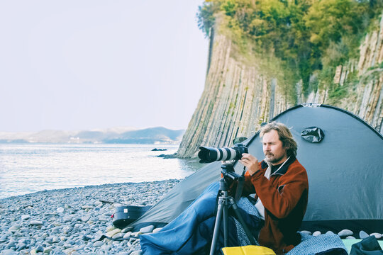 photographer tourist sits near tent on the seashore and takes pictures of landscapes