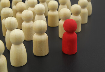 Wooden figures of people stand in rows. One red figure standing out from the crowd. Leadership and individuality concept.