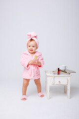 A cute little baby girl in a pink terry dressing gown with a mini dressing table and cosmetics is...