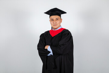 Male graduate student in mortarboard and bachelor gown on white background