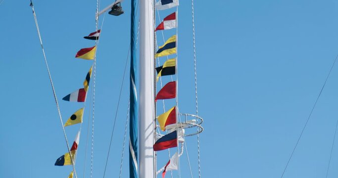 flags of different countries sway in the wind on the high mast of the yacht. The camera moves from the bottom to the top of the mast. Clear day, blue skies