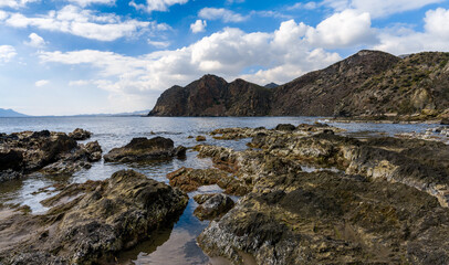 secluded rocky cove on a wild mountainous coastline with rocks and tidal pools in the foreground