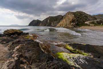secluded sandy beach on a wild mountainous coastline with colorful rocks and algae in the foreground