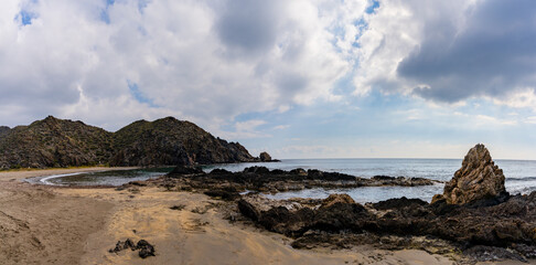 panorama view of a secluded sandy beach on a wild mountainous coastline with rocks