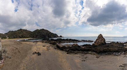 panorama view of a secluded sandy beach on a wild mountainous coastline with rocks