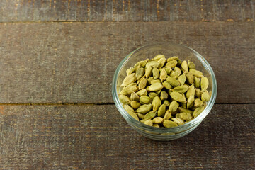 Green Cardamom on transparent glass bowl on wooden background. Green cardamom is a fragrant herb used as an ingredient for cooking. 