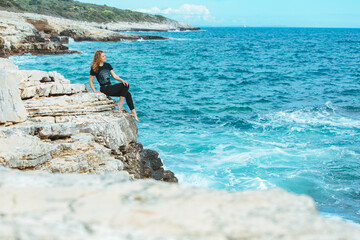 young slim woman sitting on the cliff edge looking at sea