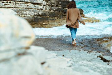 woman walking by rocky sea beach at sunny windy day. summer vacation