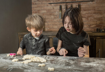 brother and sister roll out cookies from the dough and indulge in flour and playing tic-tac-toe.