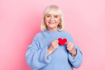 Portrait of attractive cheerful grey-haired woman holding heart card amour cupid isolated over pink...