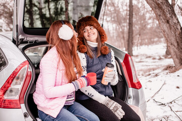 Mom and teenage daughter together. Two girls are sitting in the trunk of a car in winter. 