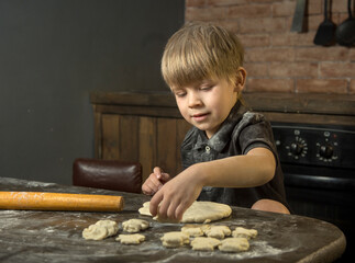 Fototapeta na wymiar a boy makes cookies out of dough in the kitchen. he holds the dough in his hands, next to a rolling pin and a mold .