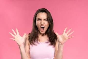 Young unhappy woman in pink female sleeveless T-shirt looking at camera with mouth open in scream and hands lifted up look isolated on pink background