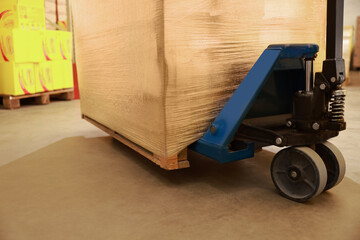 Manual forklift with wrapped pallets in warehouse, closeup. Logistics concept