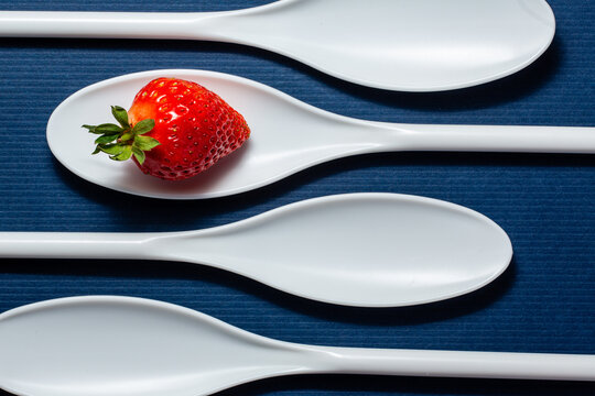 Four white spoons on a table with a strawberry