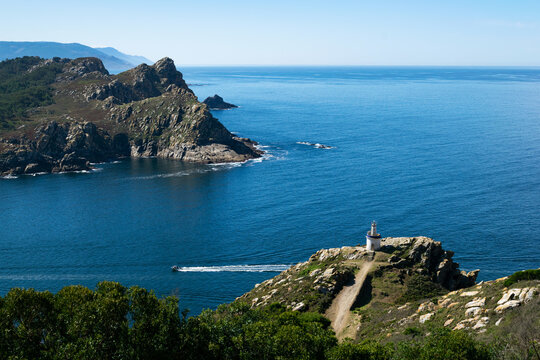 Boat sailing past a lighthouse and the south island of the Cies Islands, Galicia, Spain