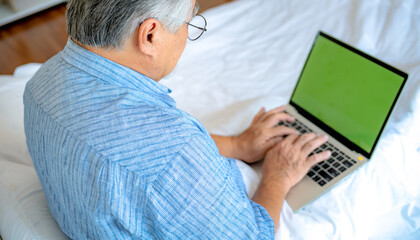 Happy old man positive, Portrait Asian Senior man and eyeglasses using computer laptop in bedroom at home, Old elderly male Technology communication retirement lifestyles concept.