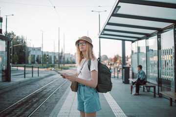 Young tourist woman hand map in outdoors at the bus stop on a city street, traveling in Europe....