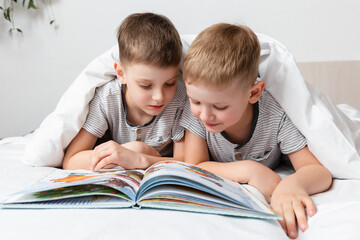 Brother's Friendship. Two cute happy children have fun, when read a book on a bed under a blanket....