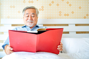 Elderly casual male or Senior man with eyeglasses reading book in bedroom at home, Mature man lifestyle concept.