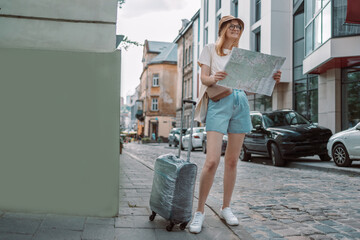 Young blonde female traveler looking for the right direction on a trip map on a city street, traveling in Europe, freedom and active lifestyle