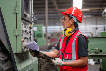 Asian male engineer in red safety vest and helmet checking and repairing old CNC machinery at factory Industrial