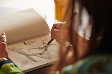 Crop artist drawing whale in sketchbook