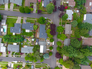 Shooting from a drone. Small green suburb. Roofs of one-story houses and industrial buildings. Lots of greenery, paved roads, car parking. Planning, construction. landscaping, design.