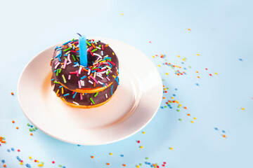 Delicious donuts with chocolate icing and birthday candle on the blue background.