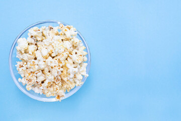 Popcorn and place for text. Blue background. Popcorn in a glass bowl for watching a movie and series. Copy space. Flat lay. Top view