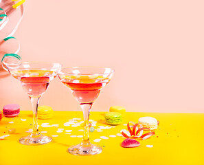 Glasses of pink cocktails with heart candies on yellow table. Birthday party or Valentines day concept.