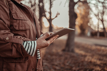 Woman hand holding digital tablet , reading news or watching online having video call using mobile application. Beautiful autumn nature background