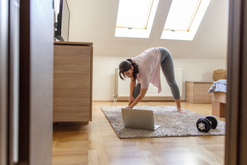 Mid-age woman doing morning exercise in her bedroom.She watching online workout lesson.	
