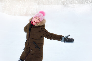 Fototapeta na wymiar A happy smiling funny child, a girl walking outside in winter, playing with snow. A sunny winter day
