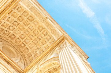 Part of a beautiful antique arch is located diagonally against a blue sky background with small clouds