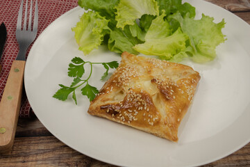 puff pastry with sesame seeds in a white plate with salad 